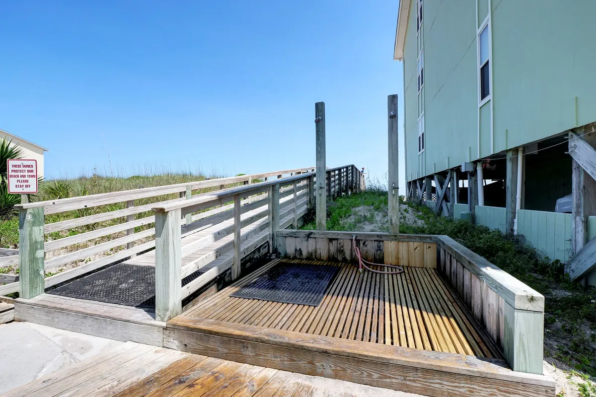 A sun-washed wooden deck bordered by lush vegetation, with an outdoor shower area visible. The relaxed atmosphere invites guests to unwind after a swim, with the deck acting as a transitional space between the interior and the serene outdoors.