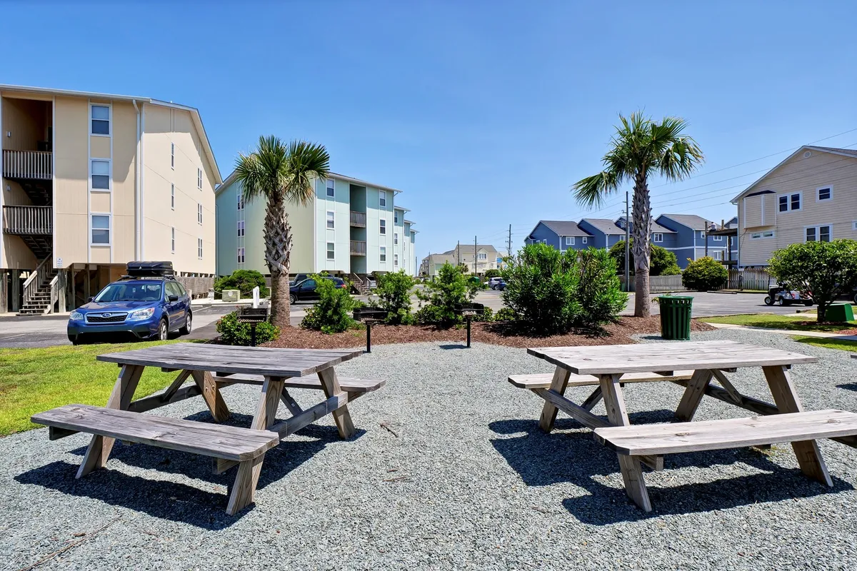 This relaxed exterior photo features picnic tables shaded by palm trees and surrounded by the condo buildings. People are seen picnicking and socializing, suggesting a friendly community atmosphere perfect for group gatherings, barbecues, and outdoor meals.