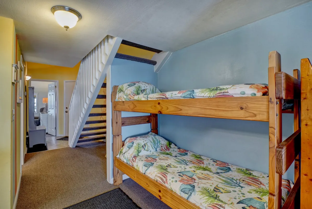 A playful yet cozy nook with twin-over-twin bunk beds set against a colorful wall, accessed by a small staircase. The space is designed for shared moments and restful nights, ideal for kids or extra guests.
