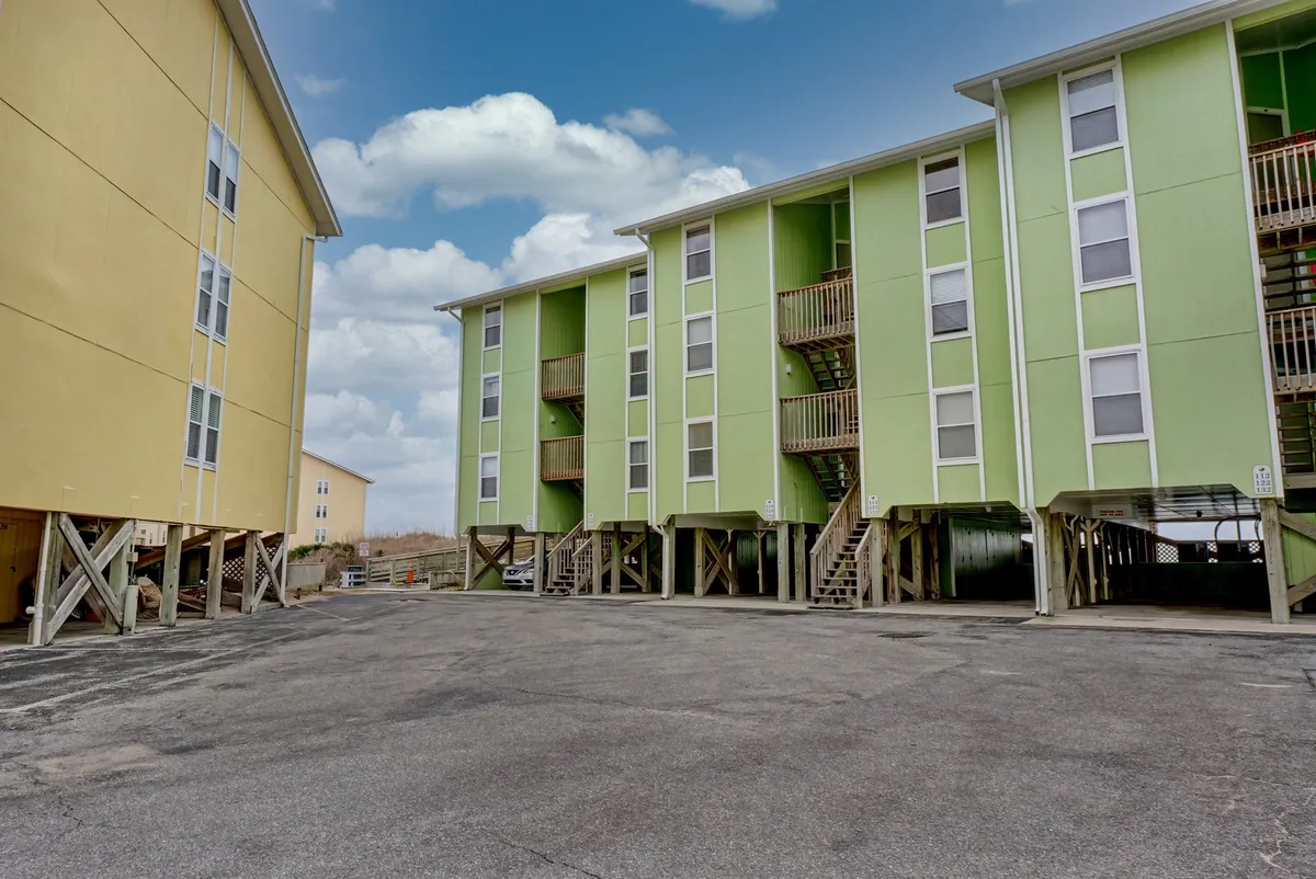 A vibrant exterior shot of the green and yellow condo buildings with steps leading up and an open parking area. The mood is cheerful, hinting at community gatherings, easy beach access, and the lively spirit of the property.