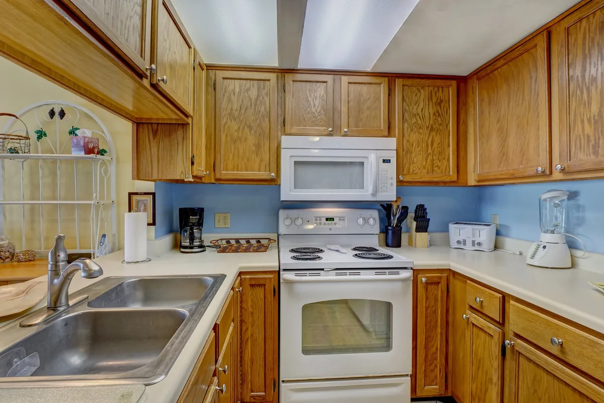 A warm and welcoming kitchen features a stainless steel sink, white stove, wooden cabinets, and a calming blue wall. The scene conveys a homey, practical space ready for everything from daily family meals to special occasions.