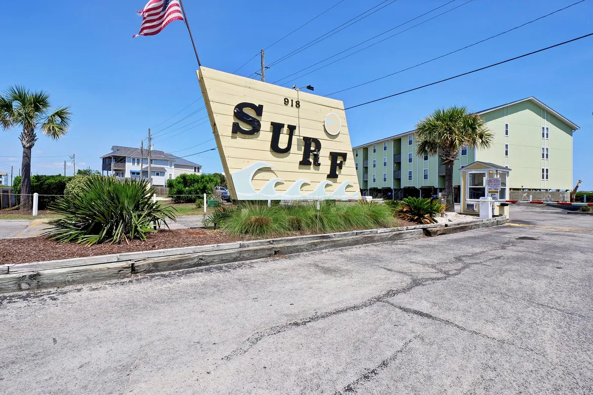 The exterior of the building featuring a prominent 'SURF' sign, framed by palm trees and inviting architecture. The scene conveys a cheerful, coastal vibe, hinting at the property’s location near the beach and local amenities.