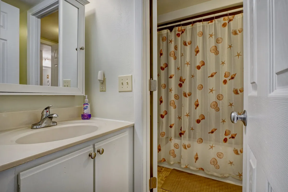 A bright bathroom space with a modern vanity, sink, mirror, and a shower curtain, designed for functionality and comfort. The layout provides the convenience of a shared but private bathing facility.
