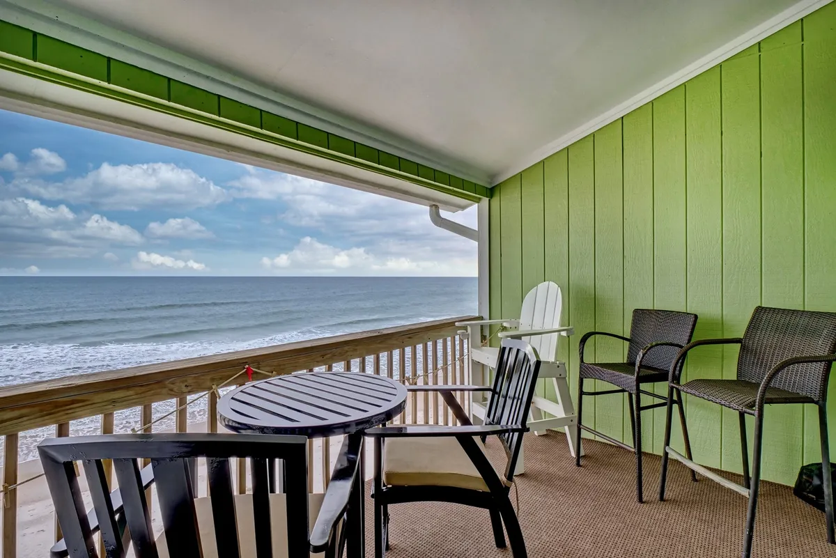 An inviting outdoor space with stylish green walls, comfortable outdoor furniture, and expansive ocean views. The setting suggests leisurely evenings, barbecues, or relaxing together after a beach day.