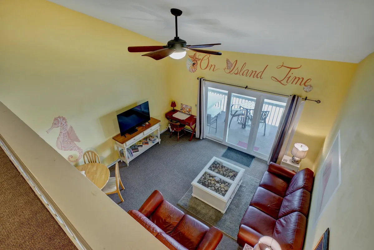 An open-plan living and dining room featuring comfortable leather sofas, colorful wall decor, a television, and sliding glass doors that lead to an outdoor space. The area feels bright, vibrant, and perfectly suited for both relaxation and entertaining.
